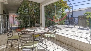 A covered outdoor patio with a round table and chairs, surrounded by potted plants and a hammock. - Apartments Anita (Slatine)