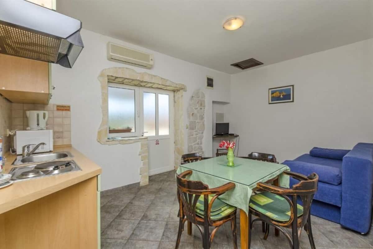 A compact kitchen with a dining area, a blue sofa, and a stone wall.