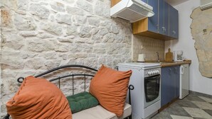 A compact kitchen with a stone wall, a bed with orange pillows, and a white stove. - Apartments Anita (Slatine)