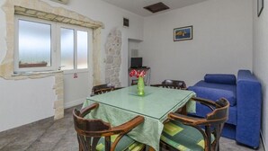 A dining area with a glass table, wooden chairs, a blue sofa, and a stone wall. - Apartments Anita (Slatine)