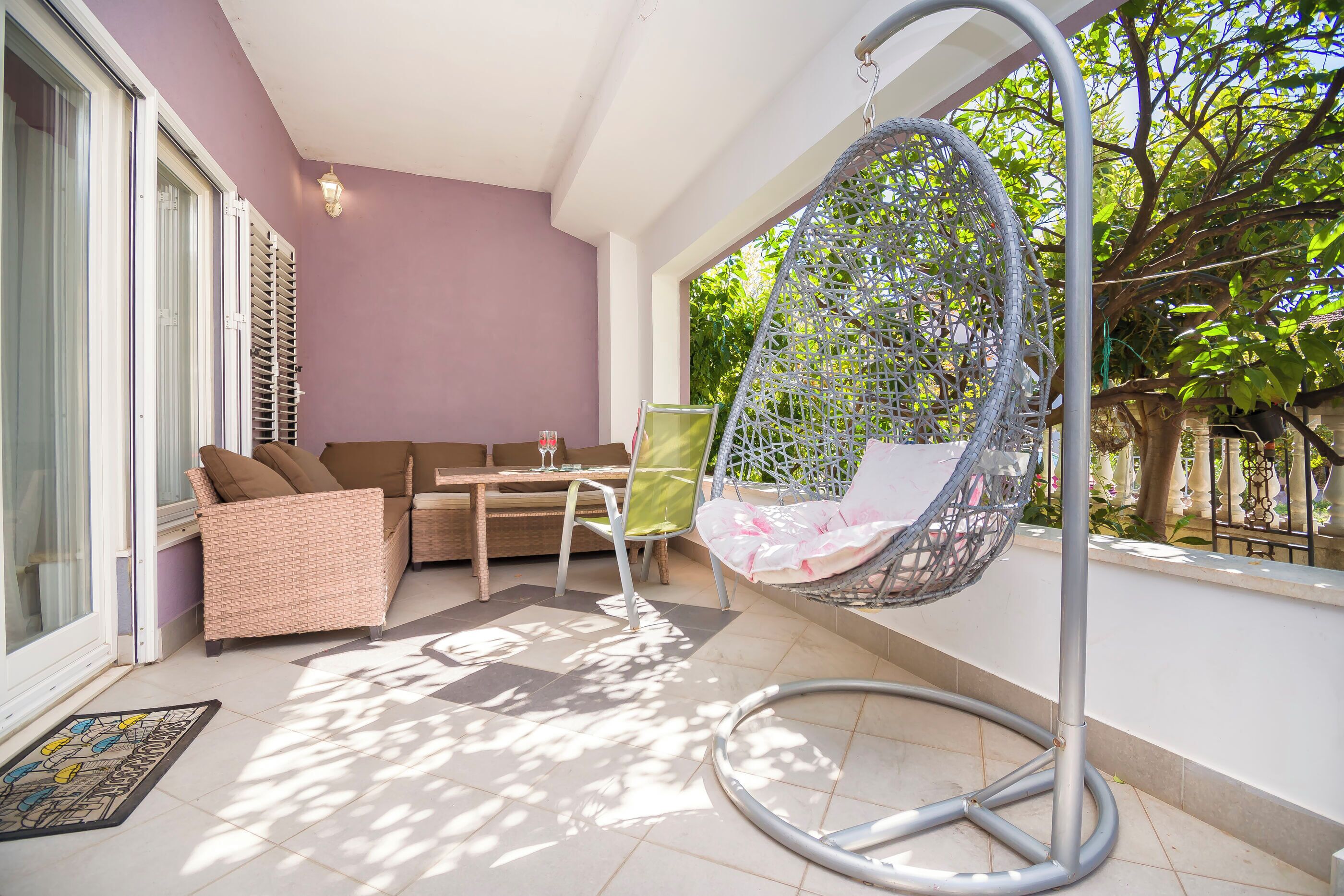 Un patio iluminado por el sol con un sofá de mimbre, una silla colgante y una mesa.