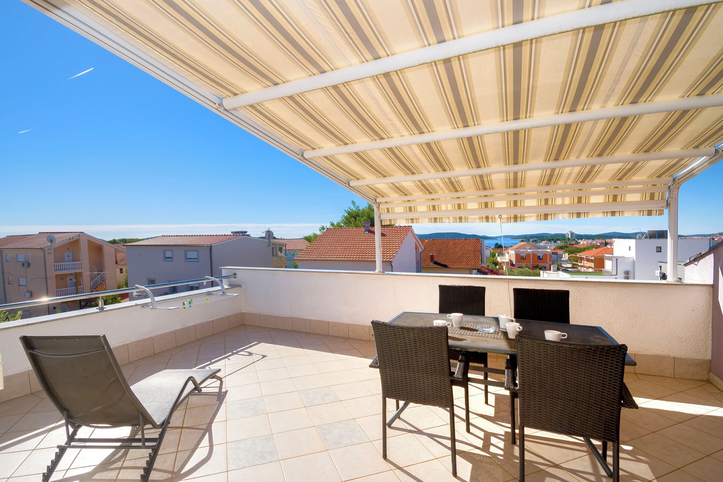 Un espacio de estar al aire libre cubierto con mesa y sillas, con vistas a un barrio residencial.