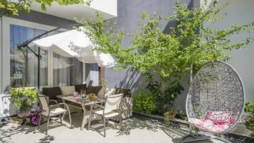 A patio with a dining table, chairs, a hanging chair, and potted plants.