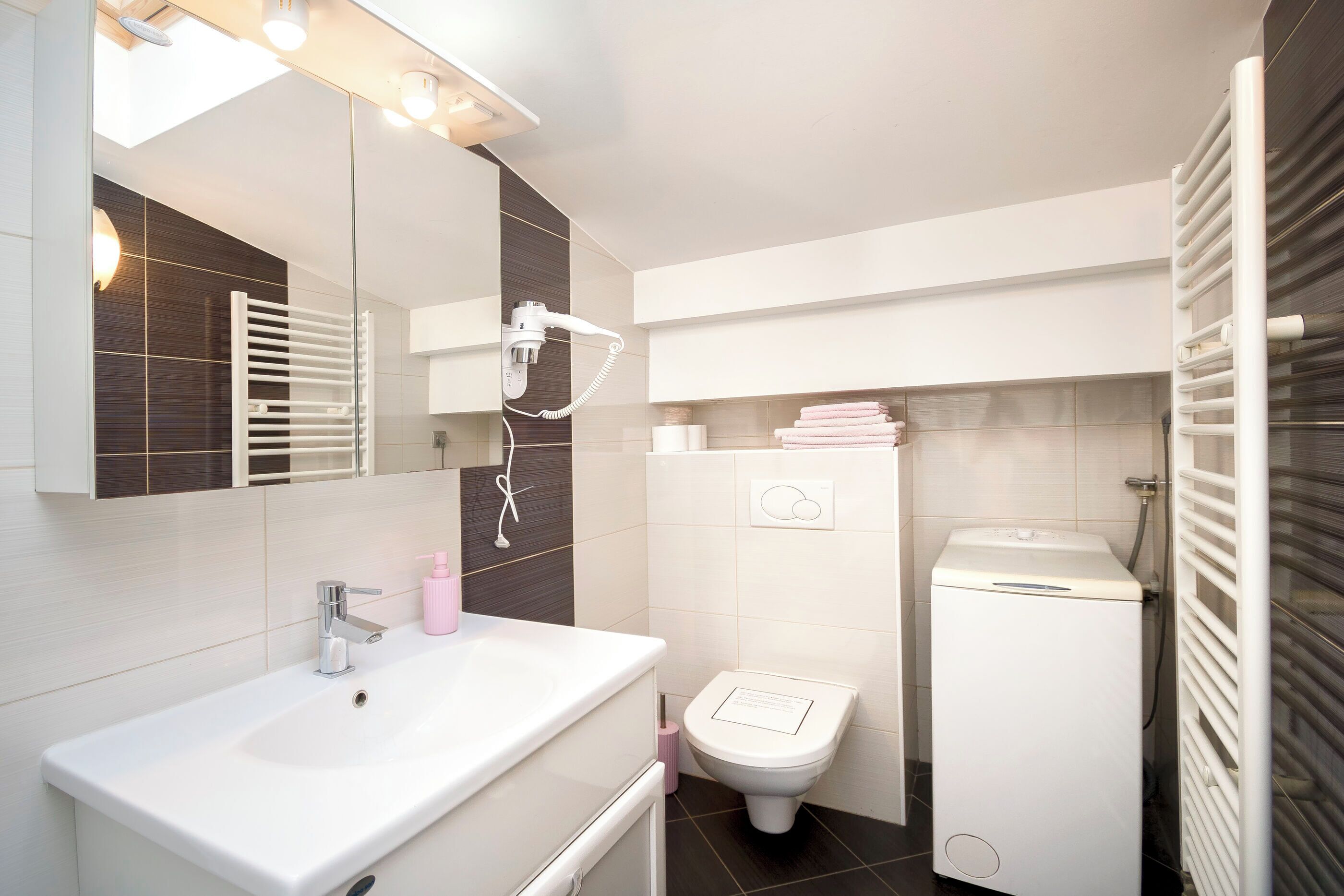 Un baño moderno con un lavamanos blanco, un inodoro, un secador de pelo y un perchero para toallas.