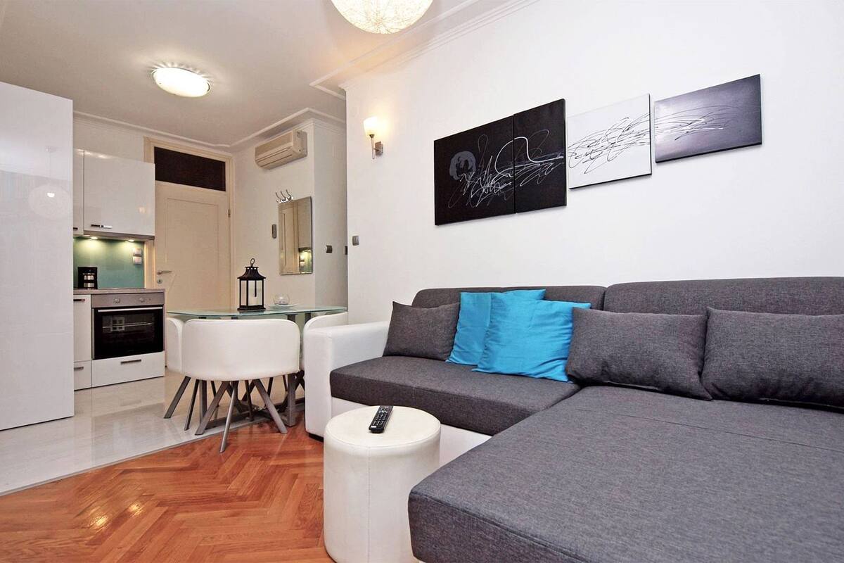 A modern living room with a grey sofa, a small round table, and a kitchen in the background.