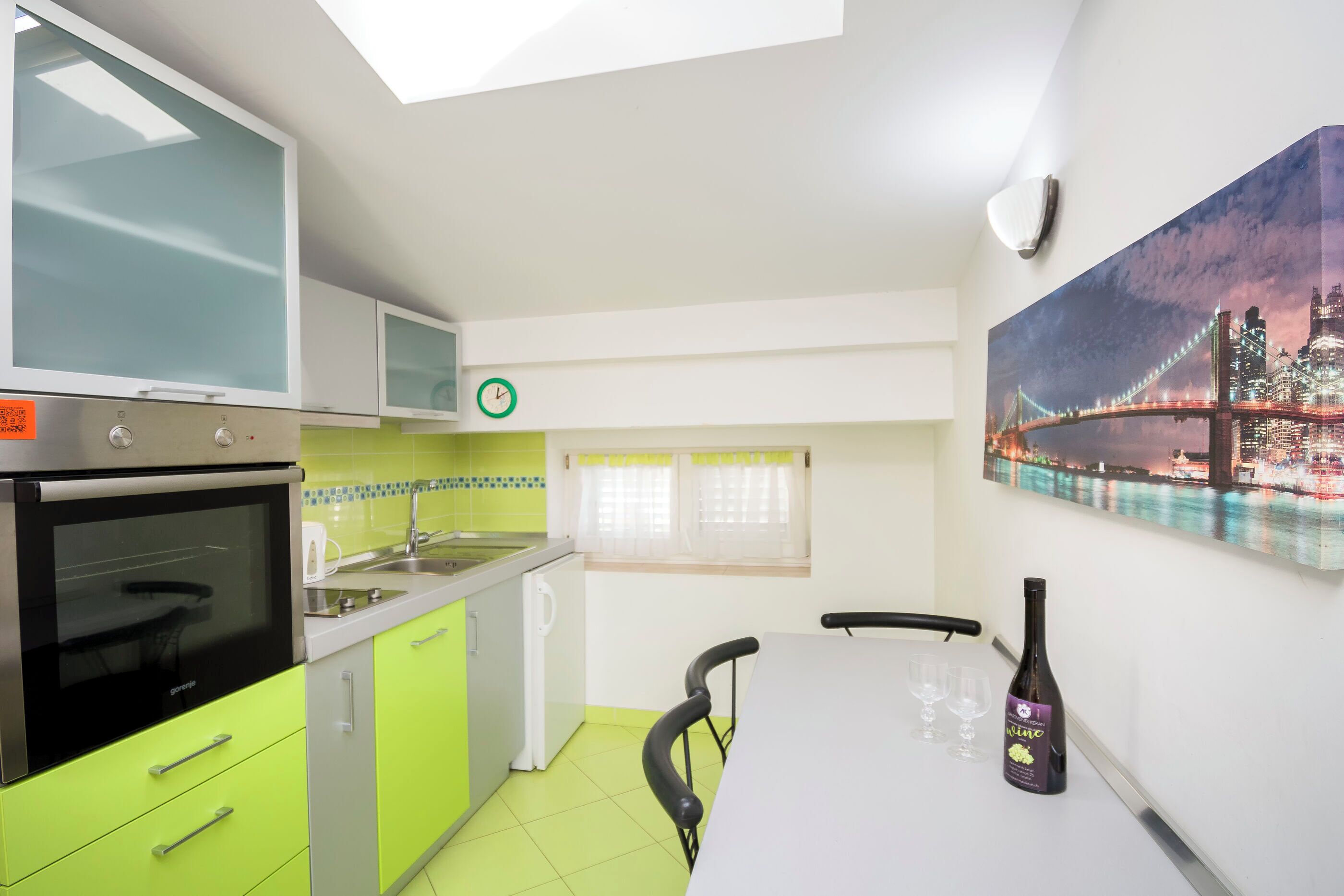 Una cocina moderna con horno empotrado, microondas y fregadero. Hay una mesa de comedor con una botella de vino y vasos.