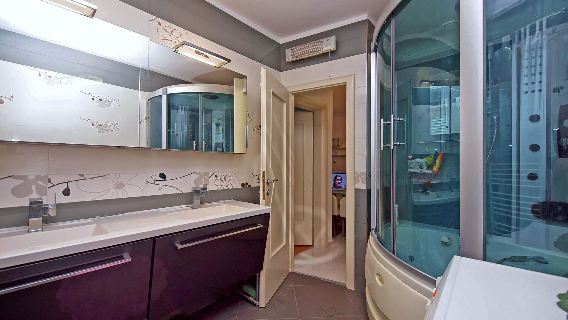 A modern bathroom with a glass shower enclosure, a vanity with a mirror, and a sink.