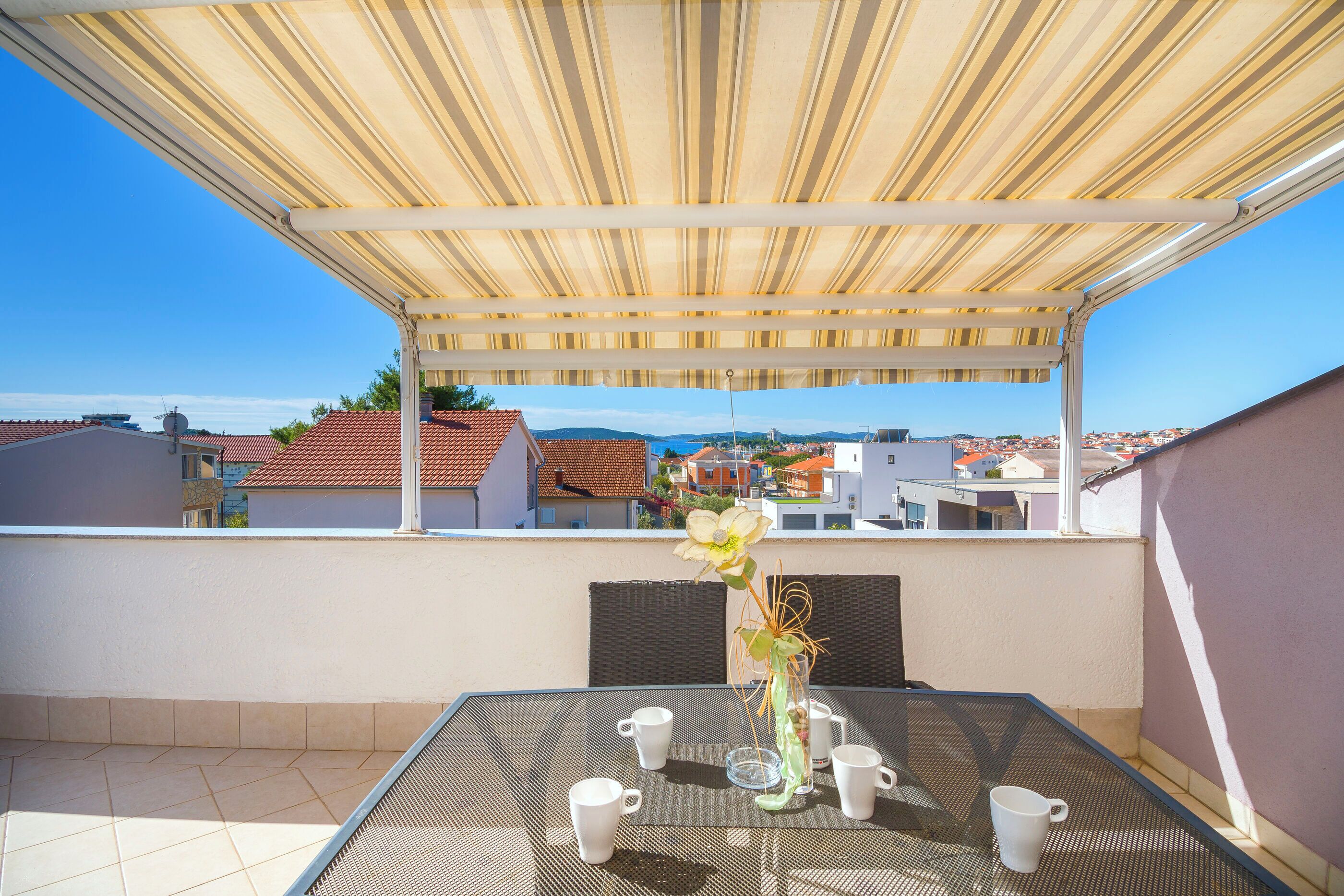 Une terrasse avec une table dressée pour quatre personnes, un auvent rayé au-dessus et une vue sur le paysage urbain en arrière-plan.