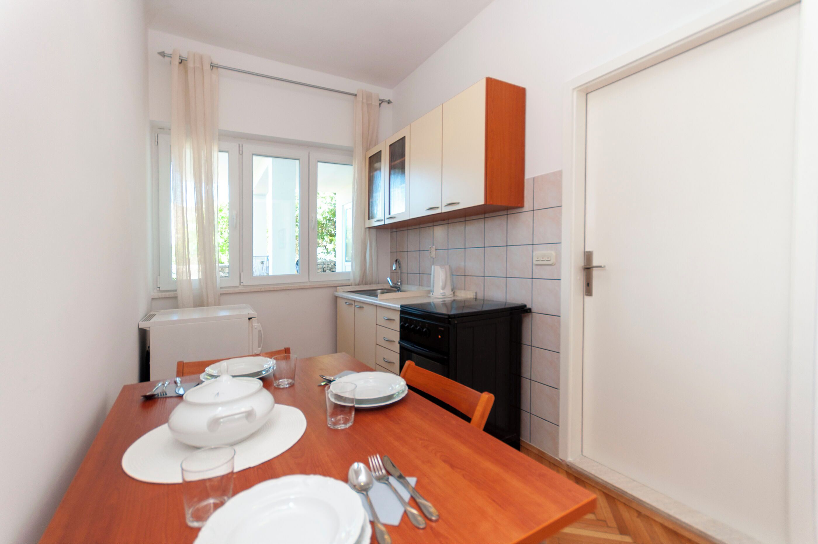 A compact kitchen with a dining table set for two, a black stove, and white cabinets.