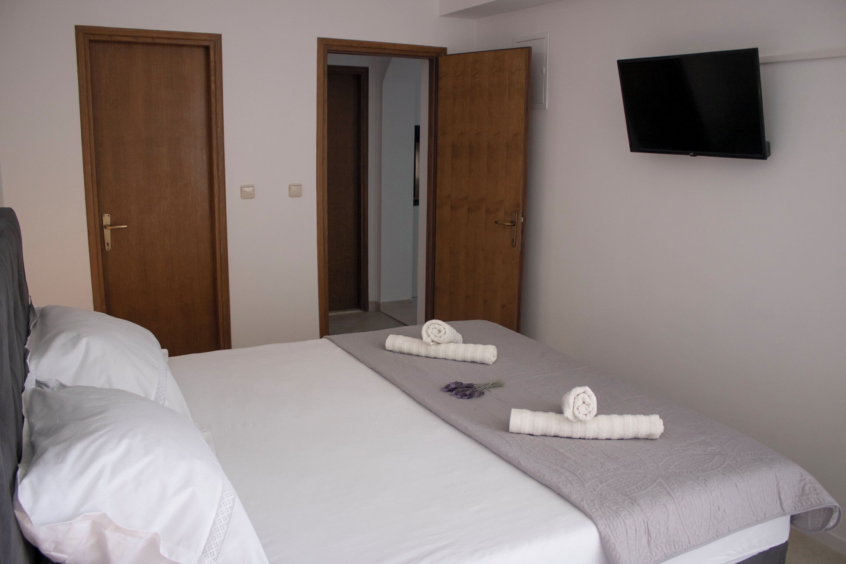 Habitación de hotel con cama, dos puertas, televisor en la pared y toallas sobre la cama.