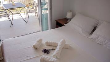 Habitación de hotel con cama, una pequeña mesa con sillas, una mesita de noche con lámpara y vistas al balcón exterior.