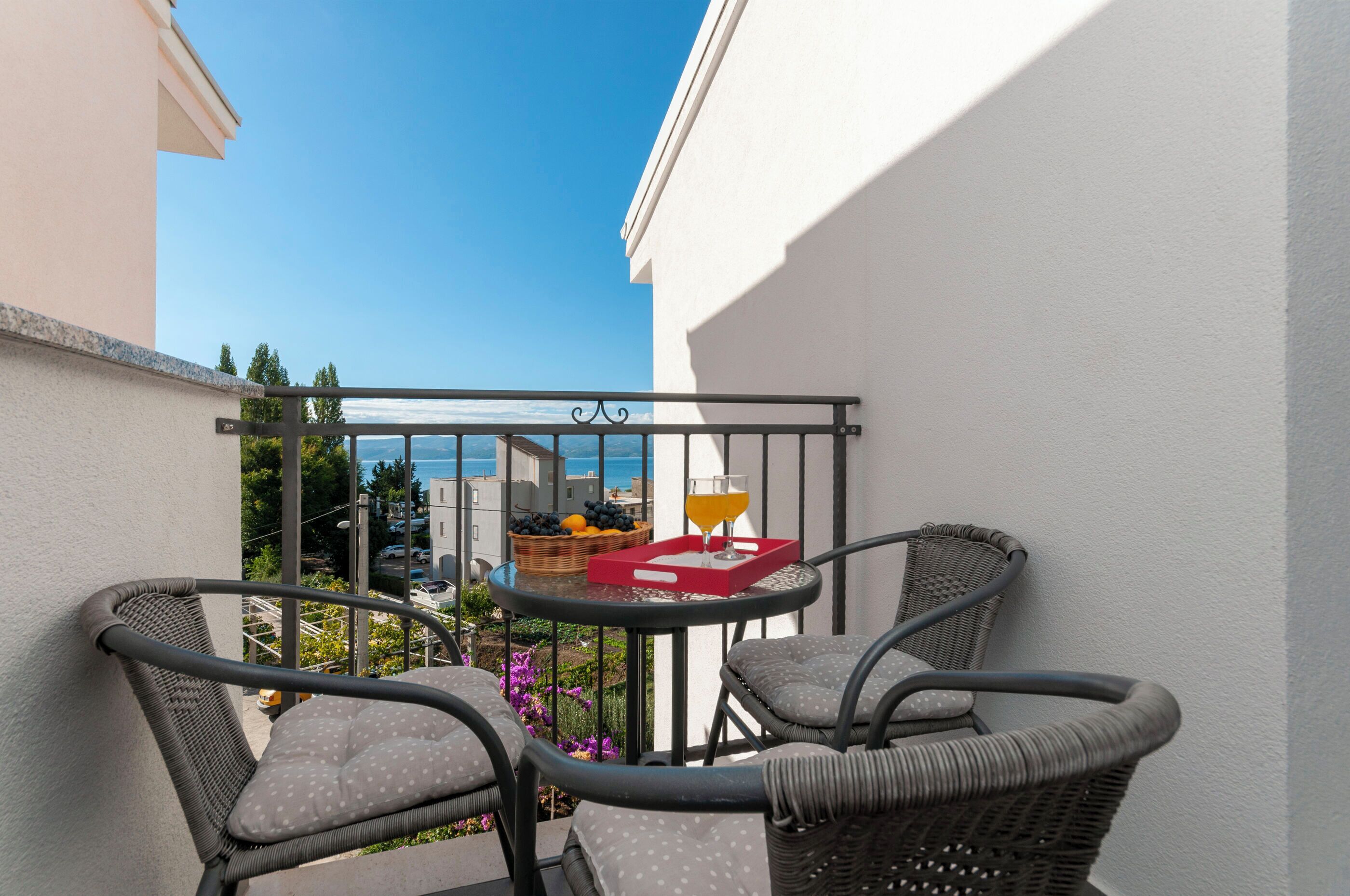 Ein Balkon mit Korbstühlen, einem Tisch, einer Fruchtkorb und einem Glas Orangensaft.