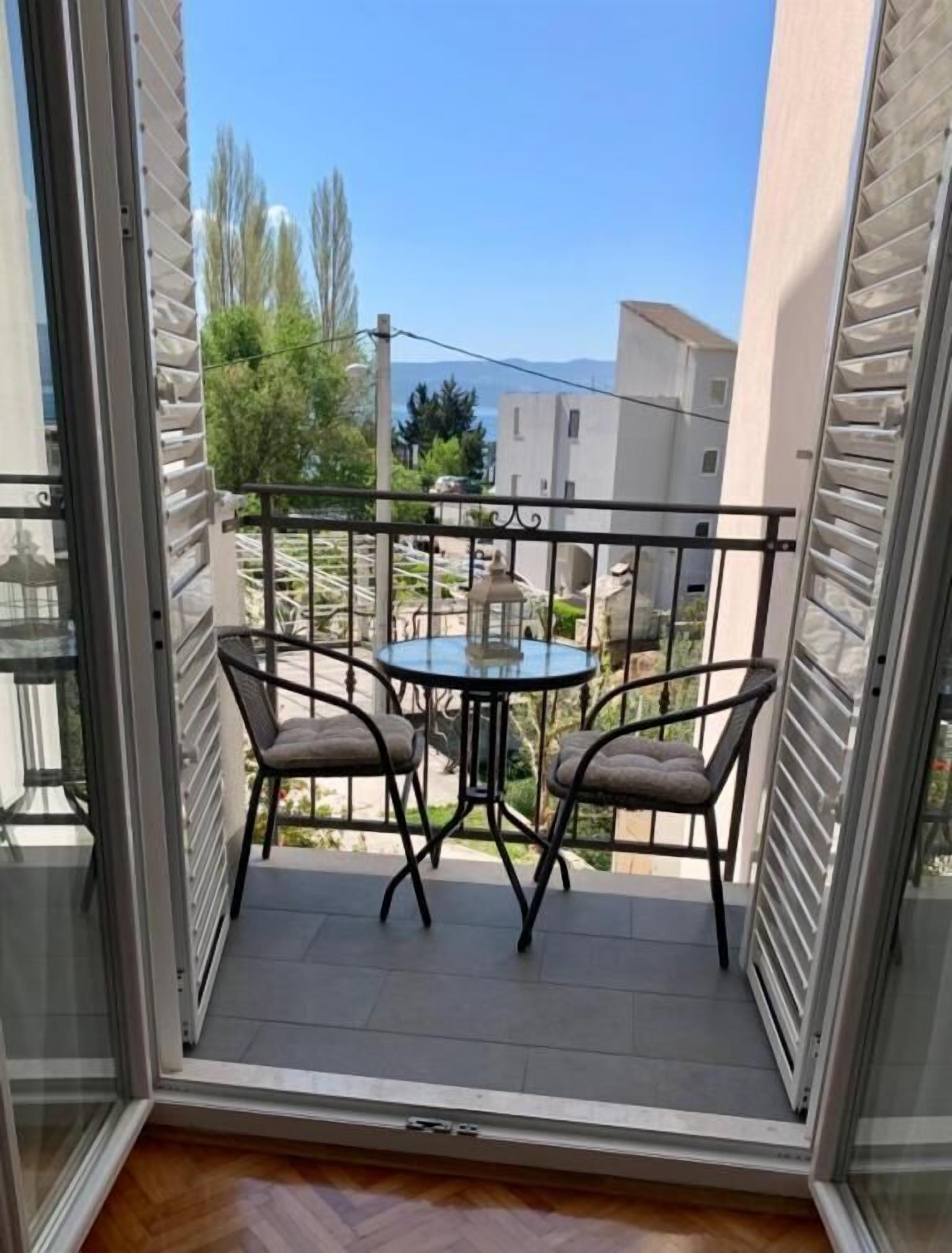 A balcony with a table and two chairs, offering a view of the surrounding buildings and greenery.
