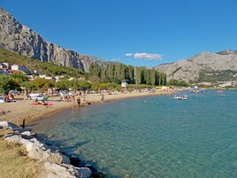 Una playa con aguas cristalinas, costa rocosa y montañas al fondo.