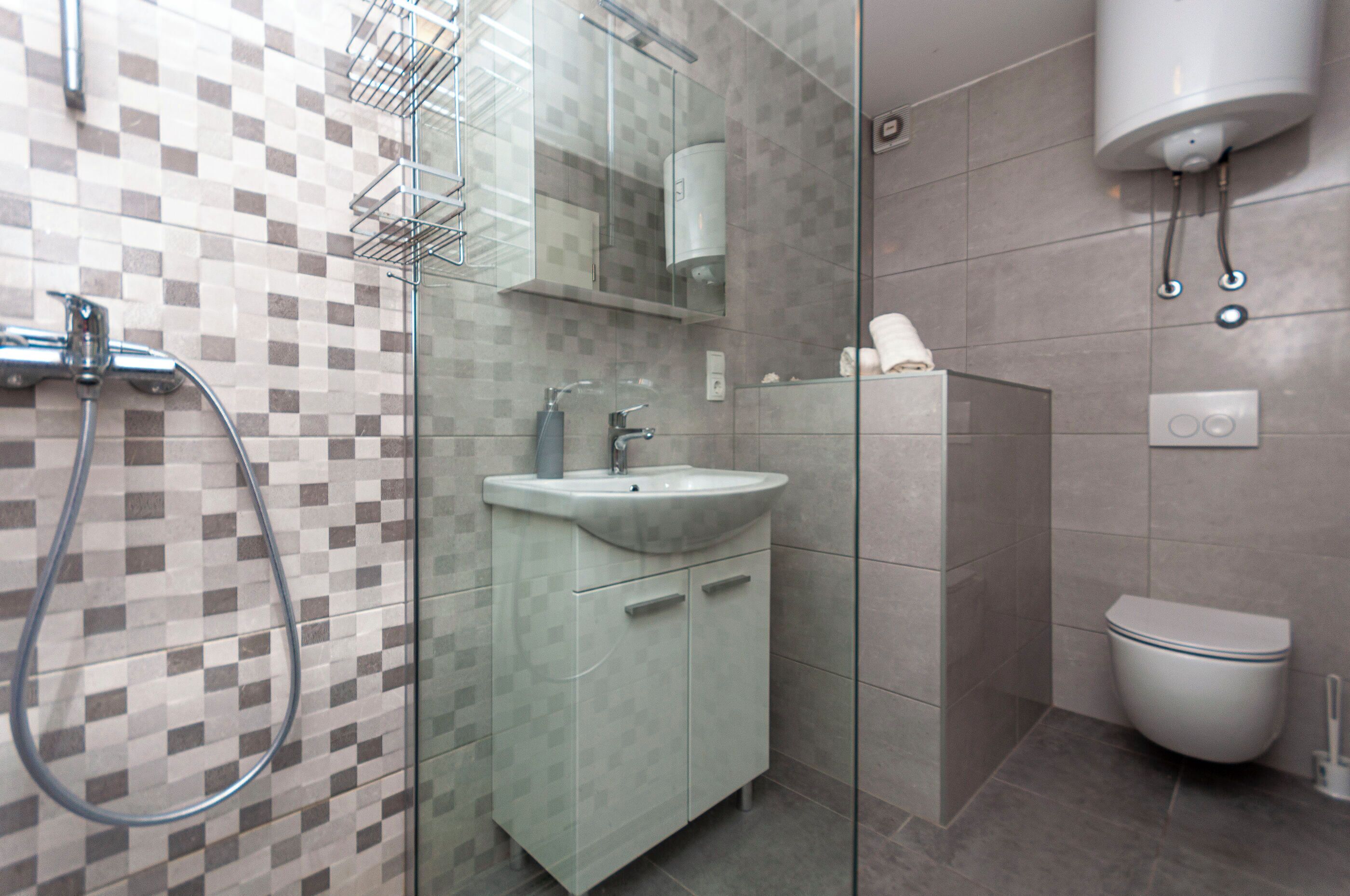 Un baño moderno con cabina de ducha de vidrio, un lavamanos con espejo y un inodoro.