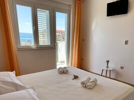Hotellihuone, jossa on sänky, pieni pöytä maljakolla ja seinälle asennettu televisio.