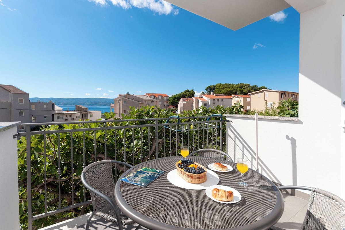 Een balkon met een ontbijttafel, compleet met croissants, een fruitmand en drankjes.