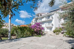 Un edificio residencial con balcones, cielo despejado y un arbusto morado con flores en primer plano.