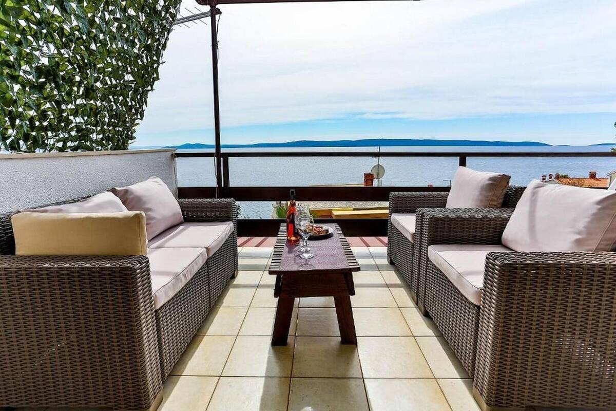 Un balcon agrémenté de meubles en osier, d’une table et offrant une vue sur la mer.
