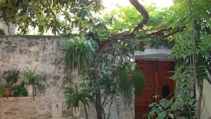 A stone-walled courtyard with potted plants, a wooden door, and a stone bench. - Apartment and Room Ivica (Trogir)
