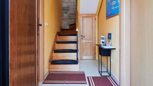 A hallway with a wooden staircase, a stone wall, a wooden door, and a small table with brochures. - Apartment and Room Ivica (Trogir)