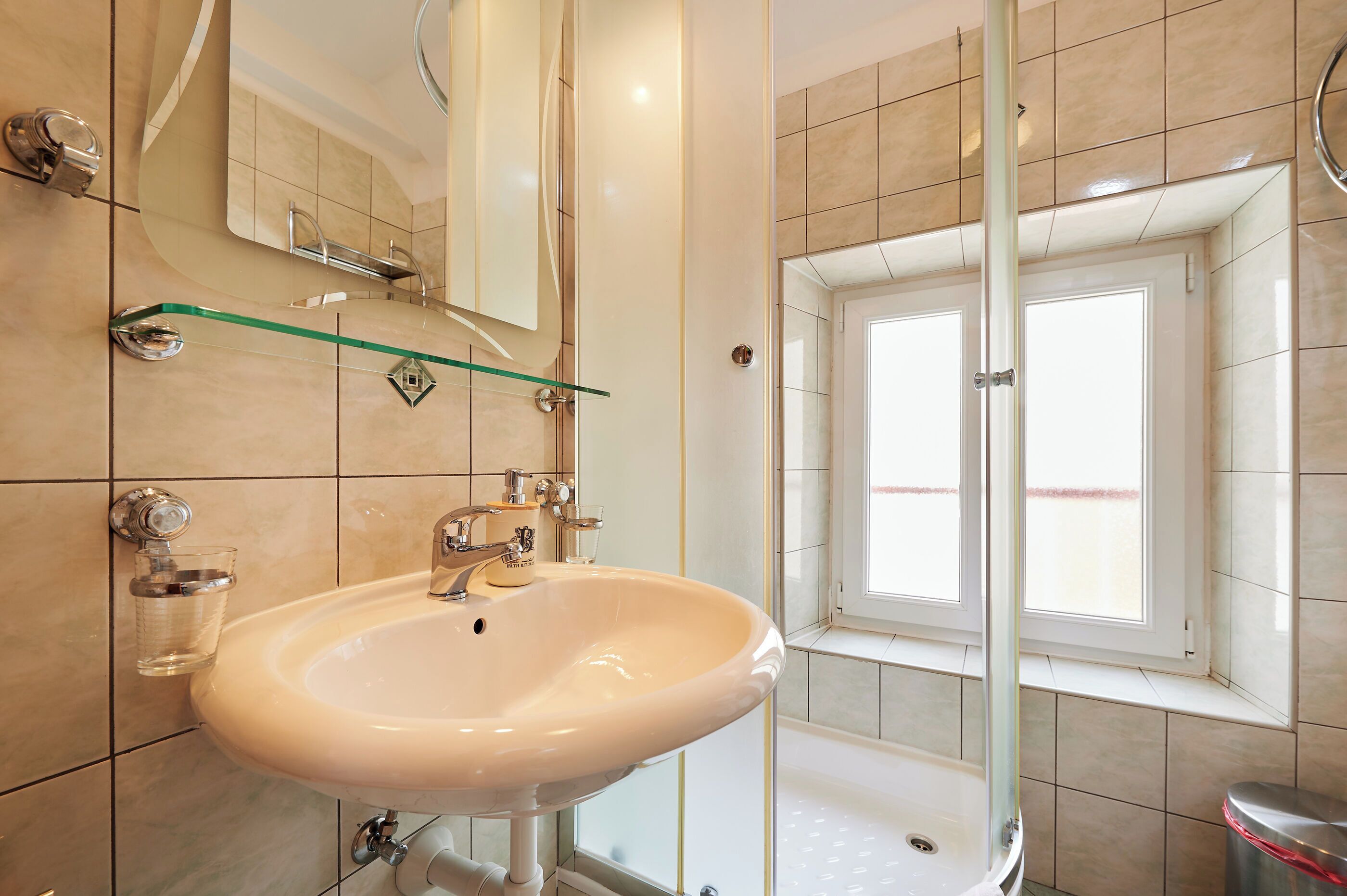 A bathroom with a sink, mirror, and window.