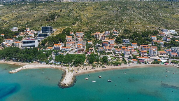 Un pueblo costero con una montaña rocosa de fondo, que presenta una mezcla de edificios residenciales y un hotel destacado.