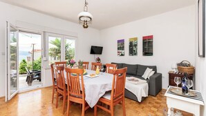 Amplia sala de estar con una mesa de comedor para cuatro personas, un sofá y un televisor montado en la pared.