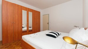 Un dormitorio con un armario de madera, una cama con ropa de cama blanca y una lámpara de noche.