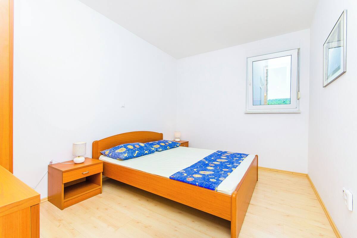 A bedroom with a wooden bed, a nightstand, a bedside lamp, and a window with a view.