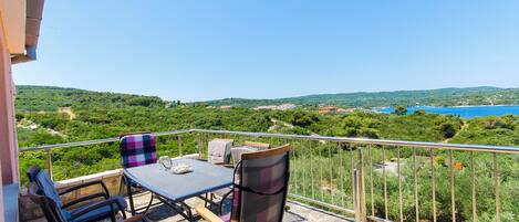 A balcony with a table and chairs, overlooking a scenic landscape with hills and a body of water.