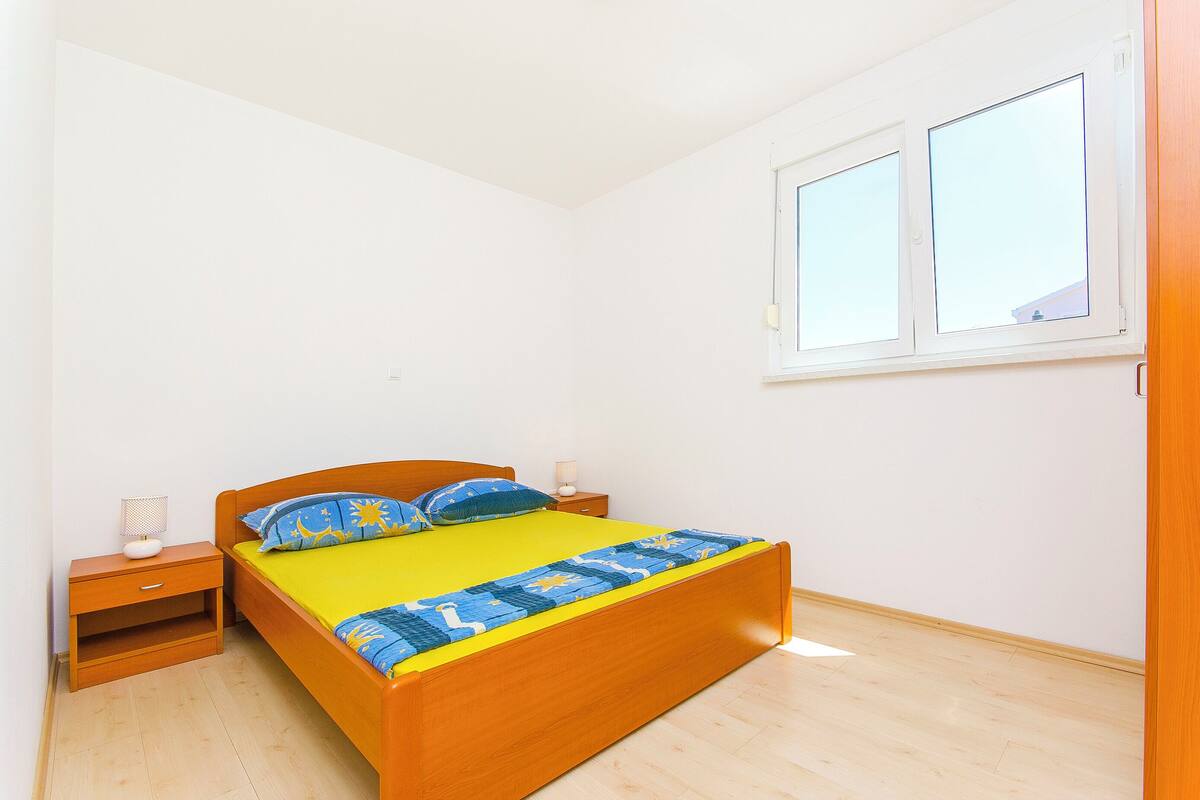 A bedroom with a wooden bed, a nightstand, a bedside table, and a window.