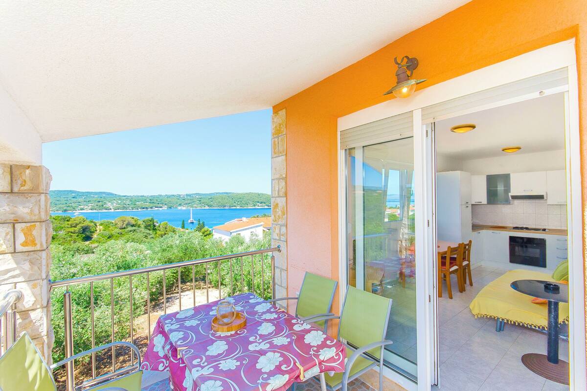 A balcony with a table and chairs, a view of the sea, and a kitchen area.