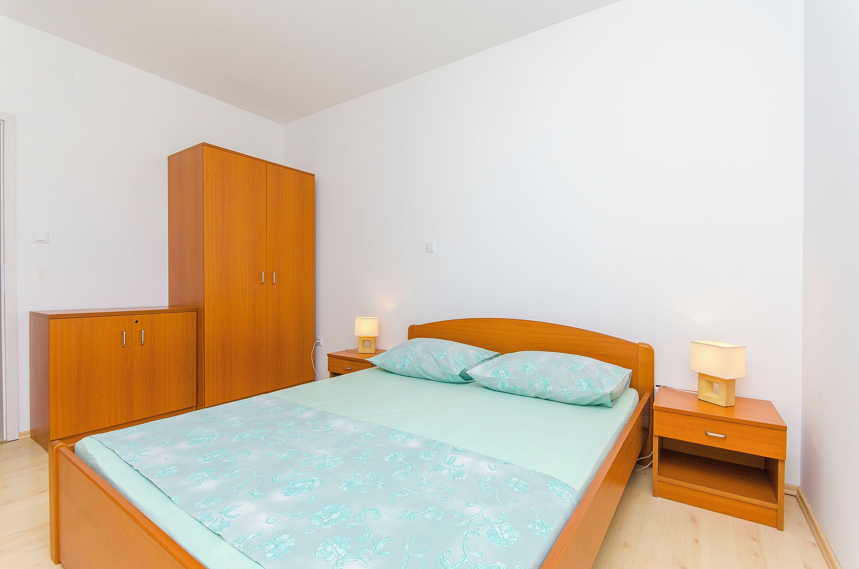 A bedroom with a bed, wooden wardrobe, bedside tables, and a nightstand.