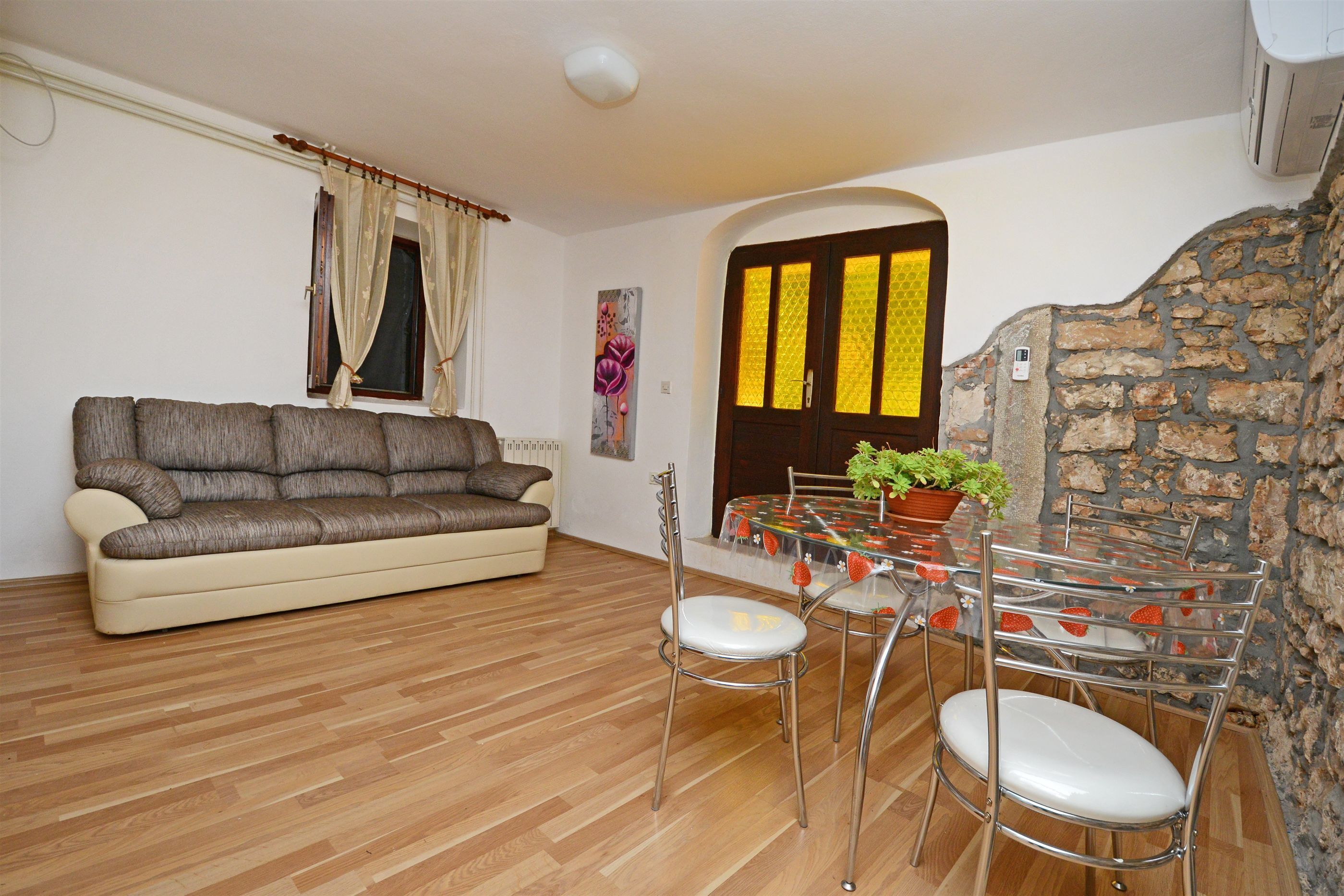 A living room with a sofa, a dining table with chairs, and a stone wall.