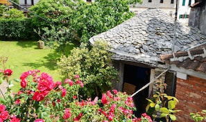 A traditional stone-roofed building with a garden featuring red roses and lush greenery.