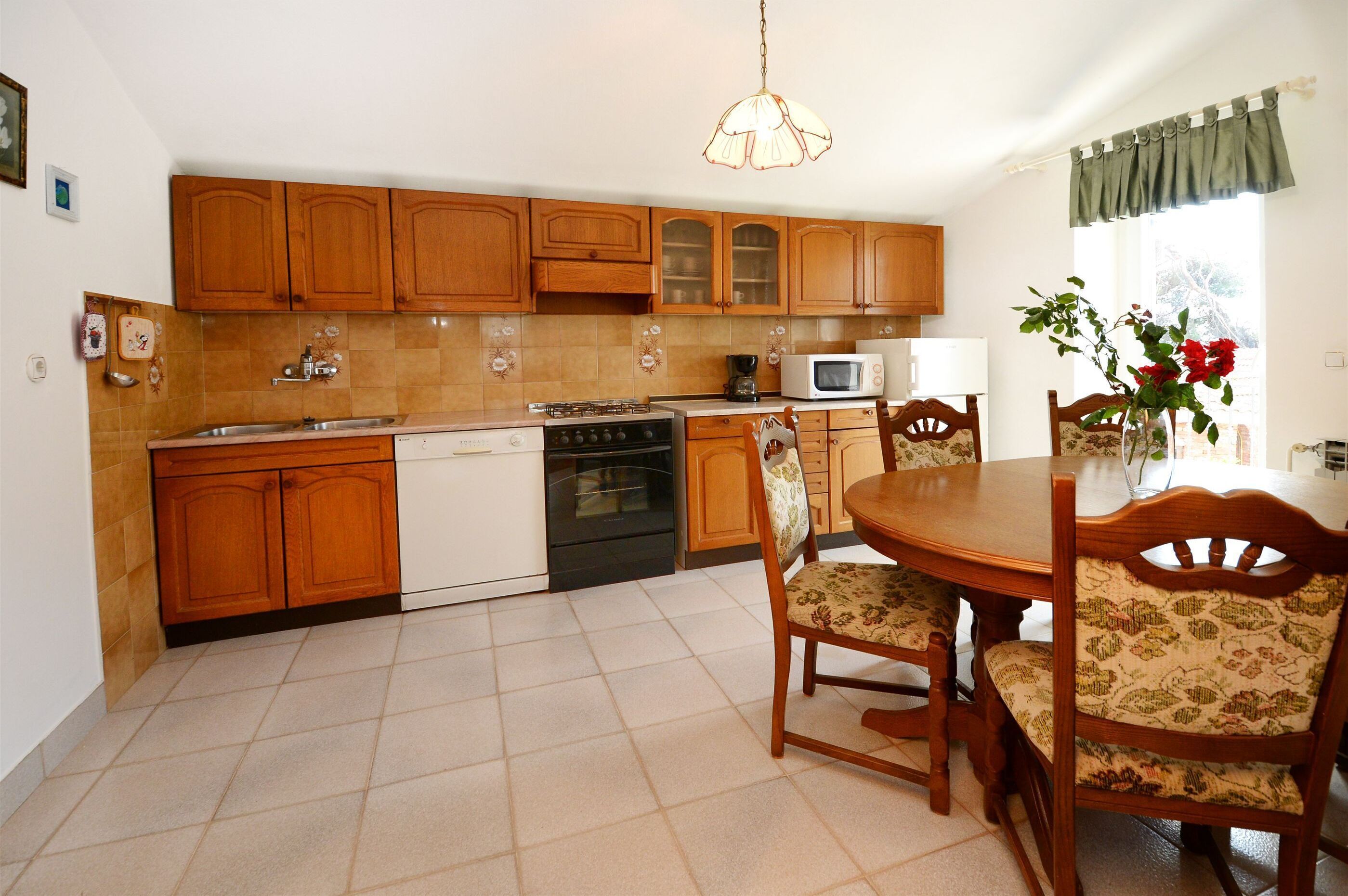 Una cocina con armarios de madera, estufa, microondas y una mesa de comedor con sillas.