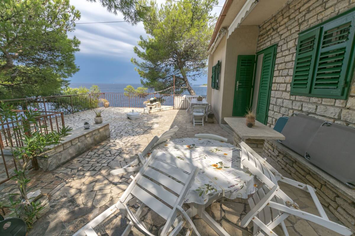 A stone patio with a white table and chairs, a stone bench, and a view of the sea.