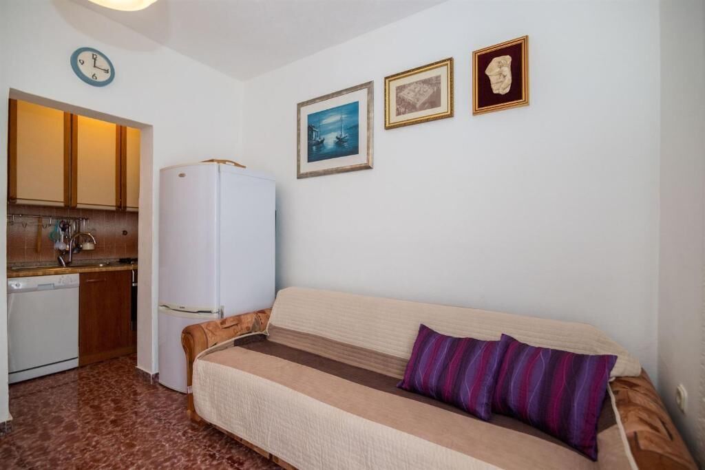 A compact room with a kitchenette, a sofa with a cushion, and three framed pictures on the wall.
