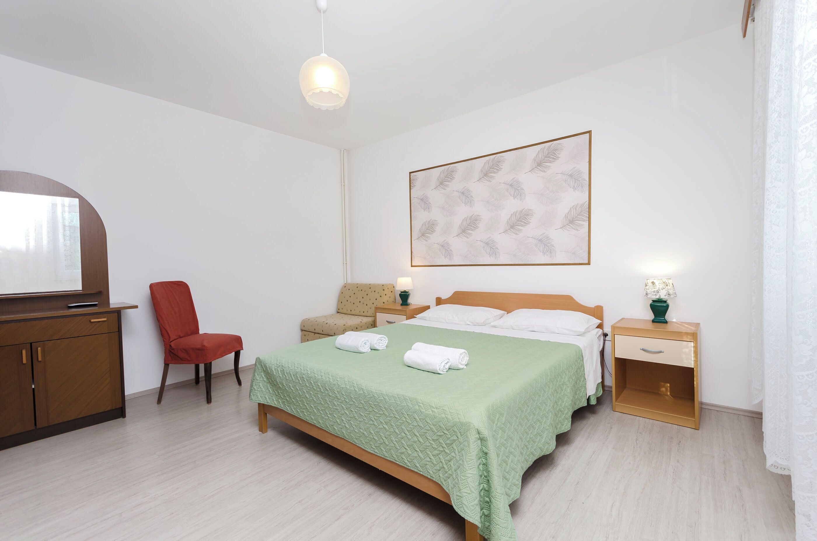Une chambre à coucher comprenant un lit, une chaise, un bureau, une table de chevet et une œuvre d’art accrochée au mur.