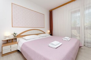 Cama bem arrumada com colcha rosa, almofadas brancas e duas toalhas dobradas ao lado.