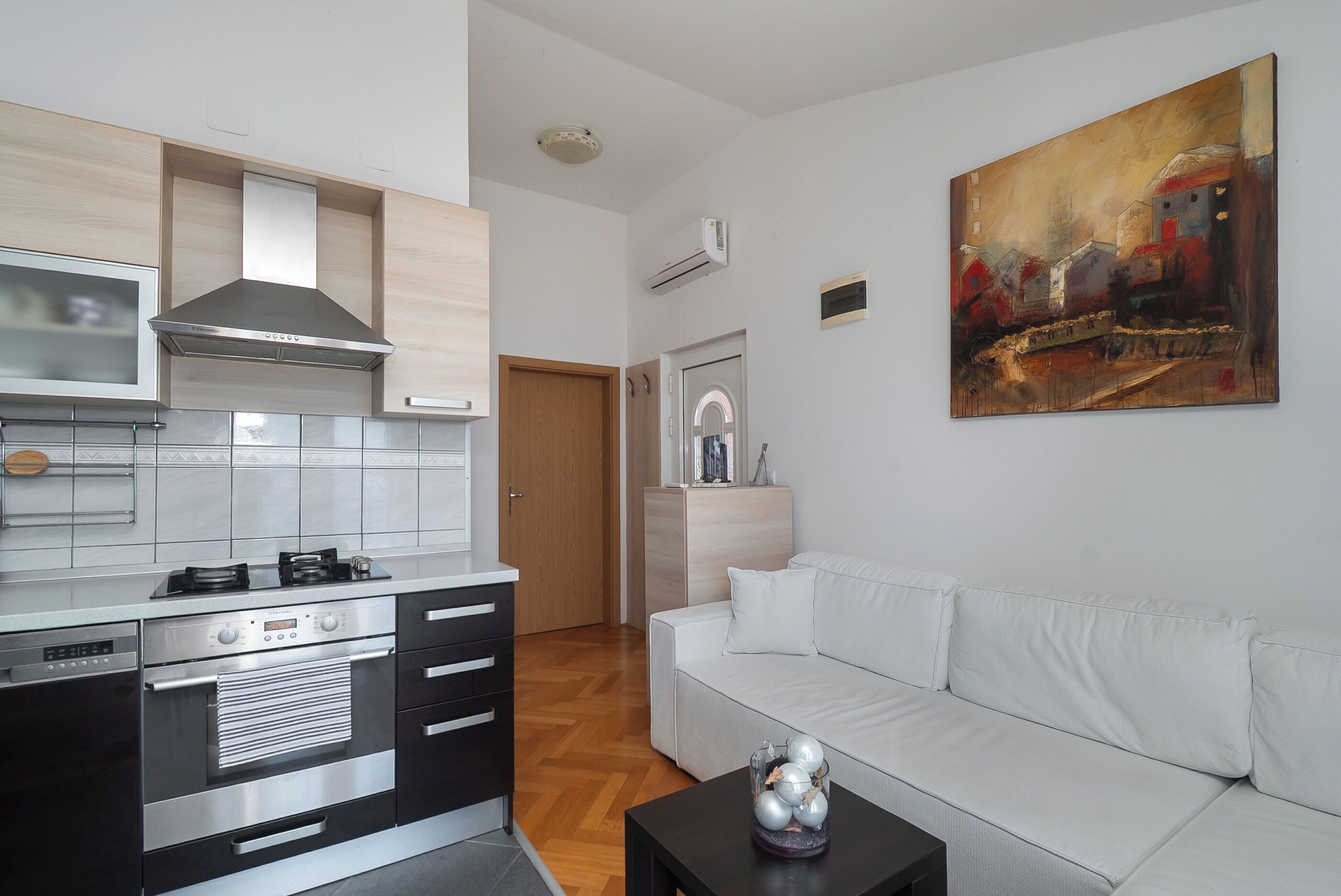 A modern kitchen with built-in appliances, a white sofa, and a painting on the wall.