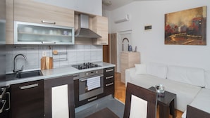 A modern kitchen with a built-in oven, a stainless steel range, and a microwave. There is a white sofa in the living area and a painting on the wall.