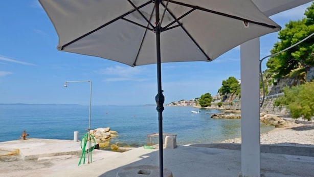 Un parasol placé à l’extérieur, sous une structure blanche, offrant une vue sur une zone côtière parée d’un ciel dégagé.