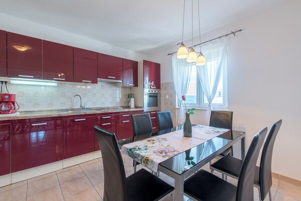 A modern kitchen with red cabinets, a dining table with chairs, and a window with curtains.