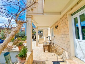 A covered outdoor patio with a stone floor, a wooden table, and wicker chairs. - Apartments Ivanka (Supetar)