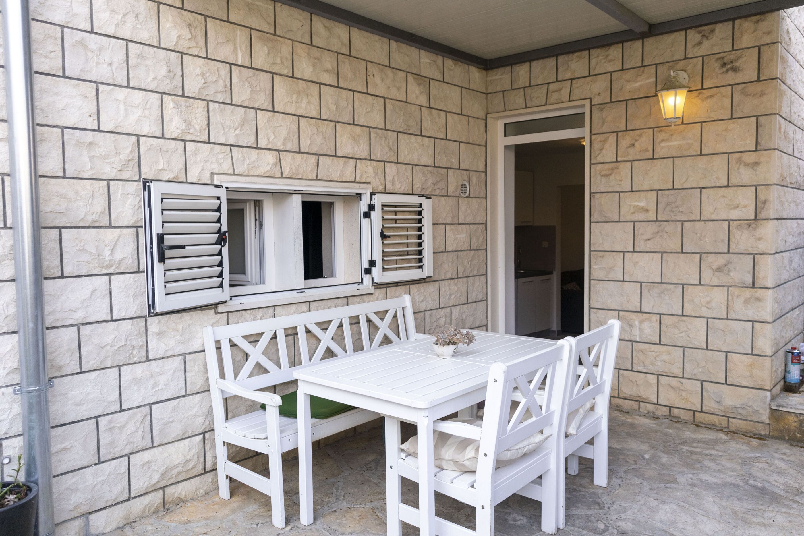 A white table and bench set against a stone wall with a door and a light fixture.
