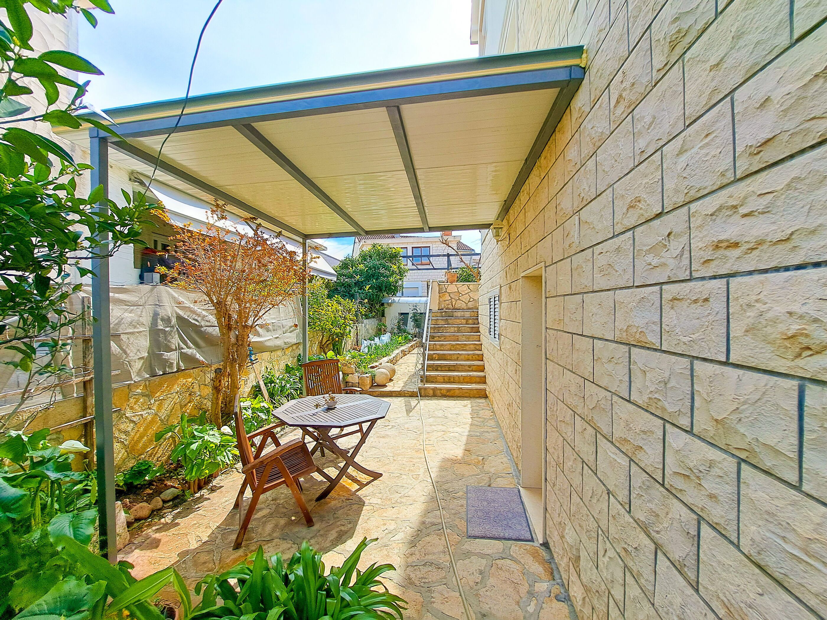 A covered patio area with a table and chairs, stone flooring, and a staircase leading to an upper level.