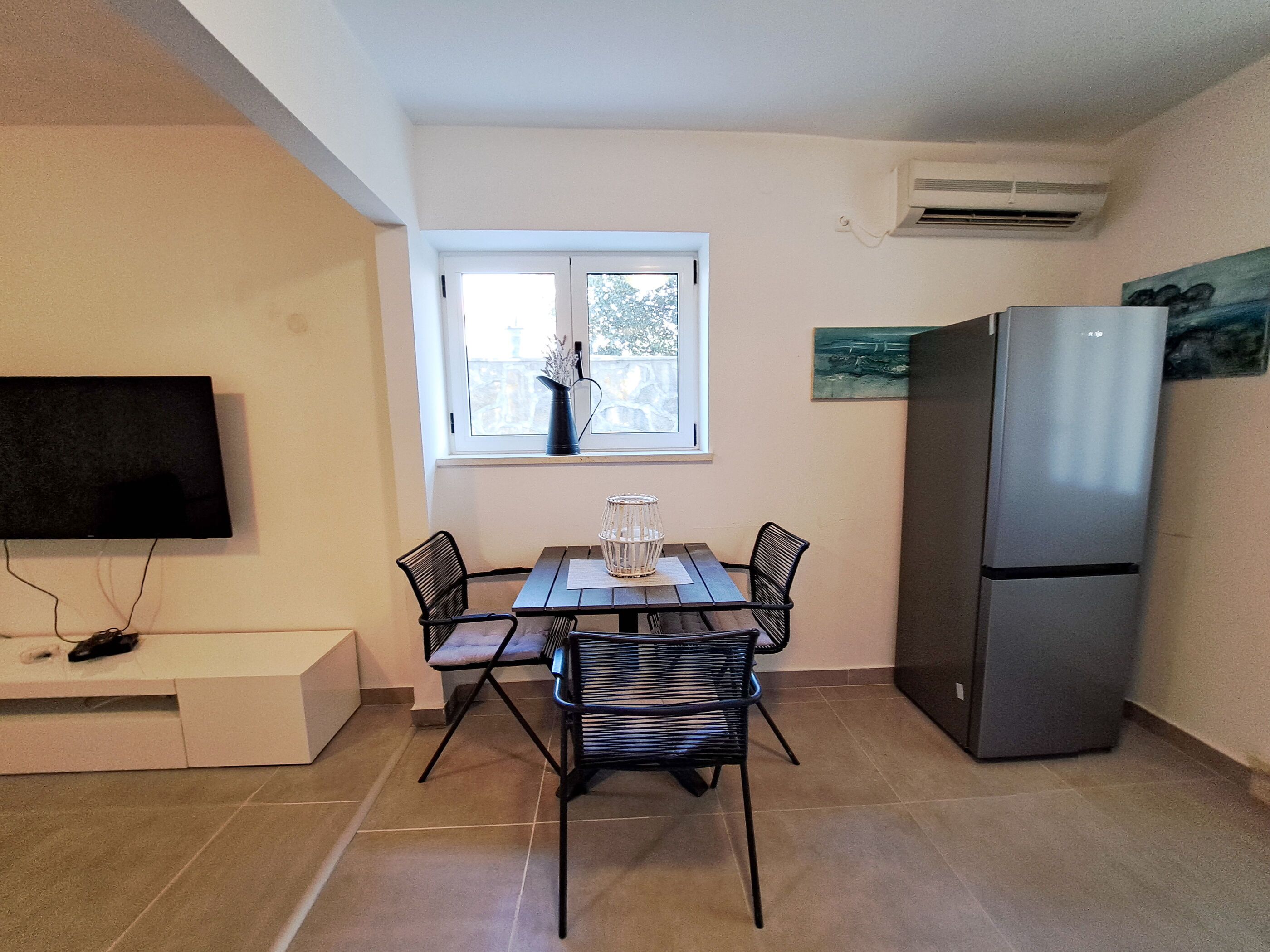 A compact kitchen with a dining table, chairs, a refrigerator, and a TV mounted on the wall.
