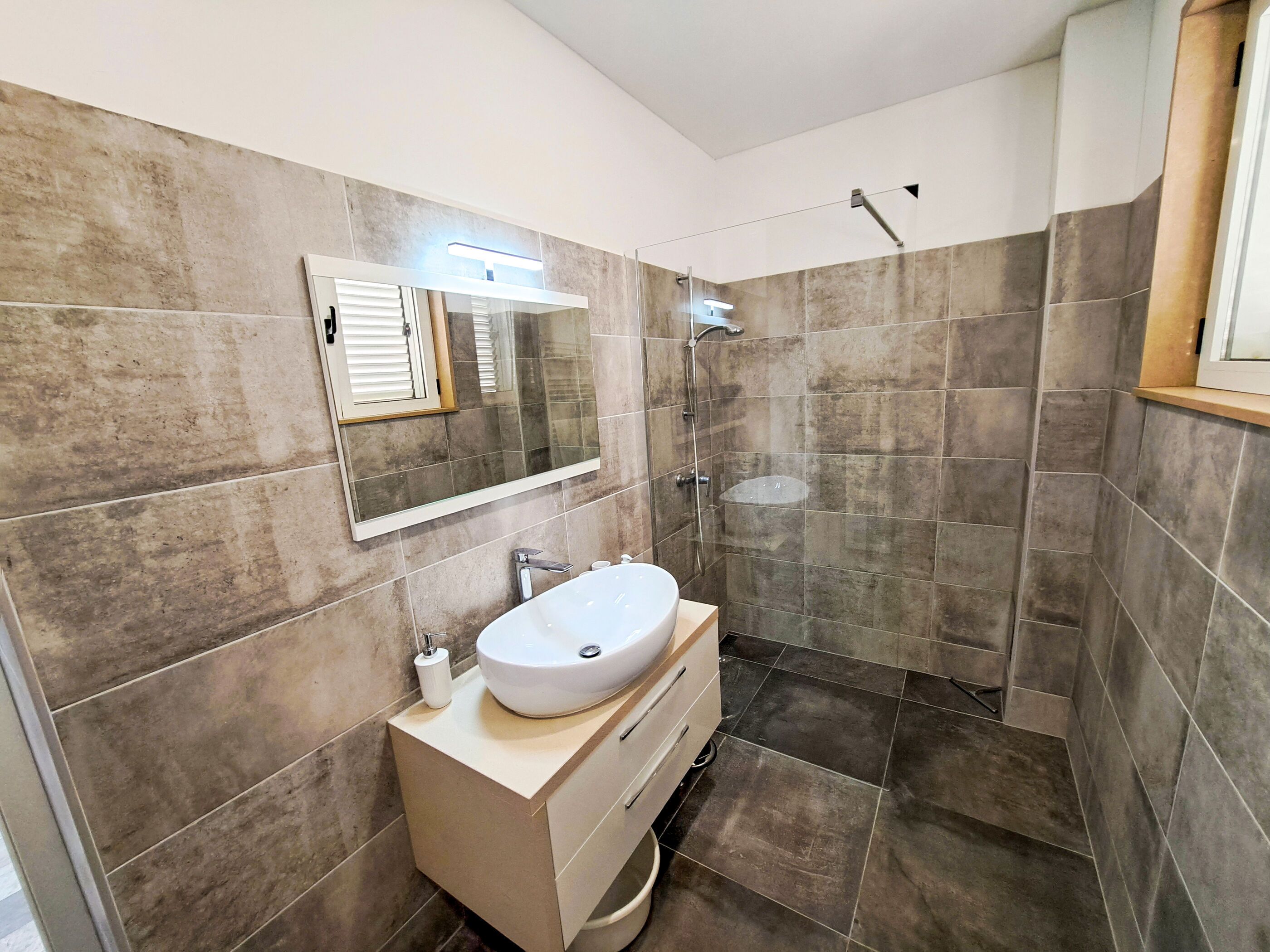 A modern bathroom with a large mirror, a white sink, and a shower area.